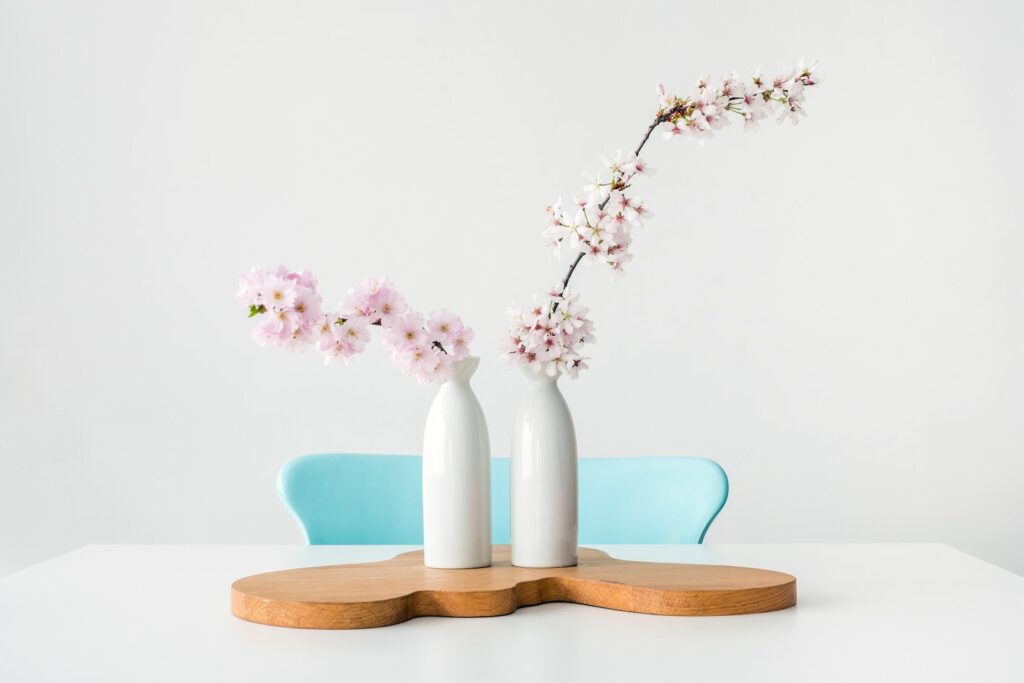 two pink petaled flowers in white vases on brown wooden surface