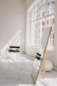 Bright minimalist room with a modern armchair, large mirror, and sunlight casting dramatic shadows.